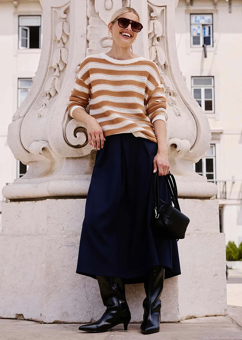 Pull en maille à rayures, jupe midi foncée et lunettes de soleil.