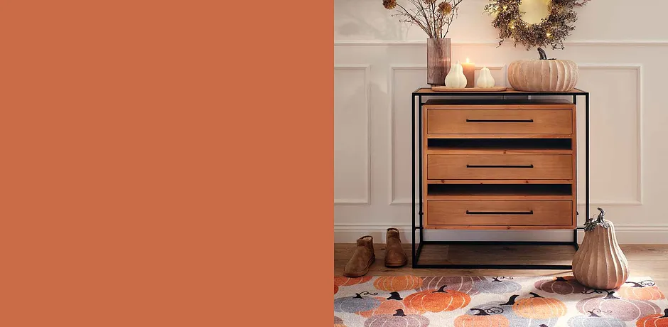 Commode en bois avec poignées noires, entourée d'objets de décoration d'automne dans des tons chauds et terreux.
