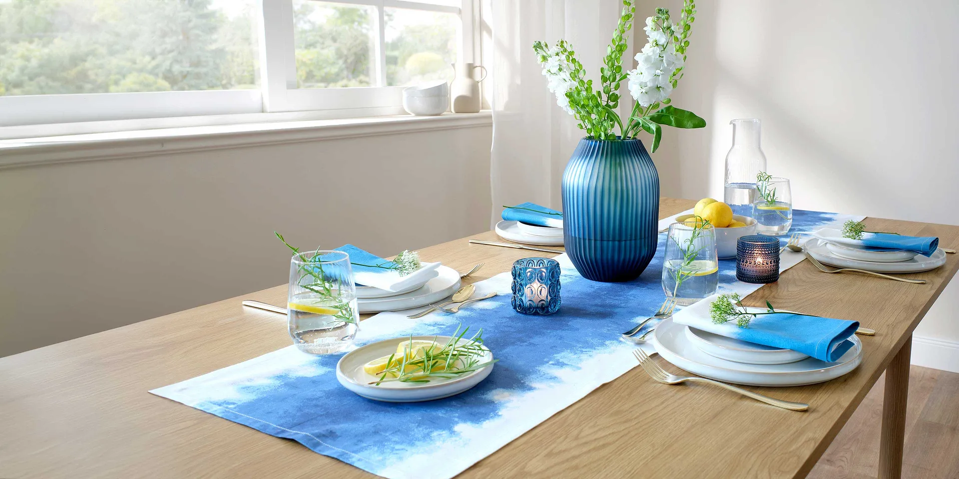 Un chemin de table bleu décore la table de salle à manger, en contraste avec des assiettes blanches et des accessoires colorés.