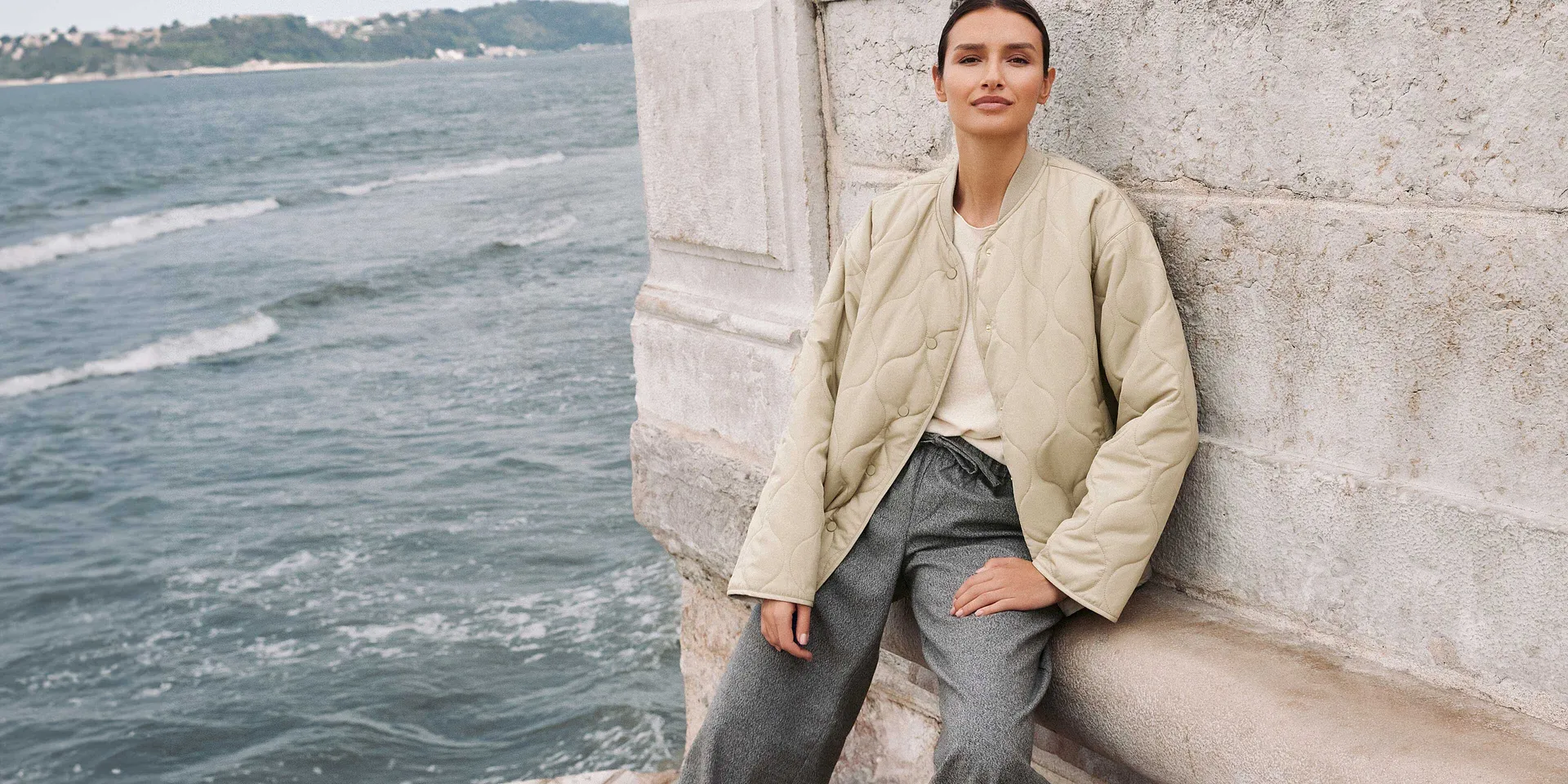 Look d'automne décontracté : veste beige, jean bleu clair et top blanc en bord de mer.