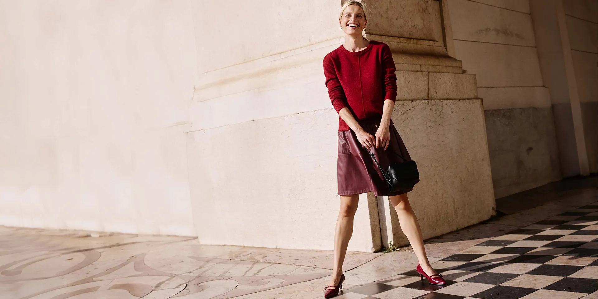 Pull rouge et jupe courte rouge, un sac noir complète la tenue.