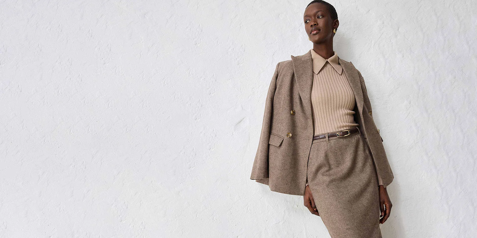Blazer de couleur beige avec un pull en maille et une jupe assortie.