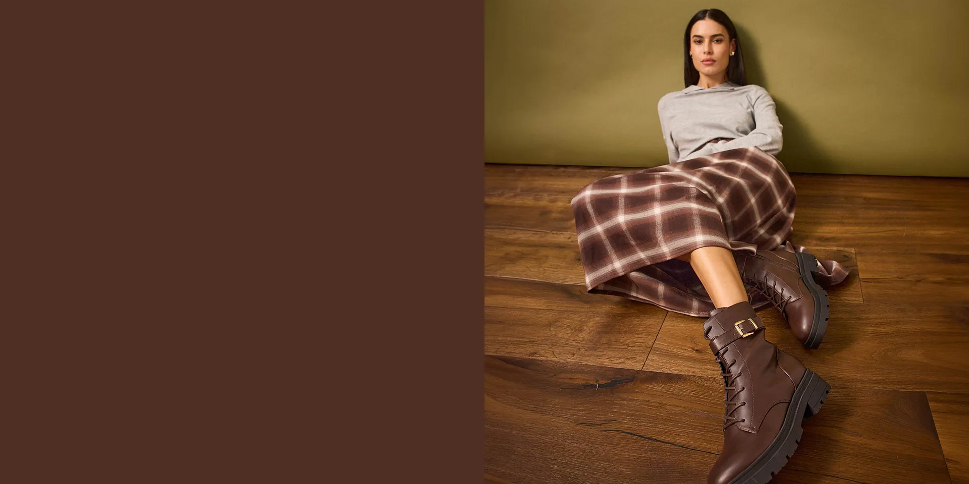 Pull gris, jupe à carreaux et bottes marron.