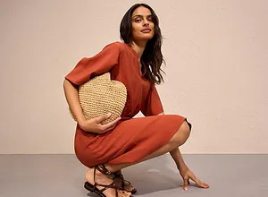 Combinaison à manches courtes orange rouille complétée d'un sac en paille et de sandales féminines.