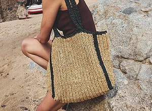 Sac de plage estival en paille avec des détails noirs.