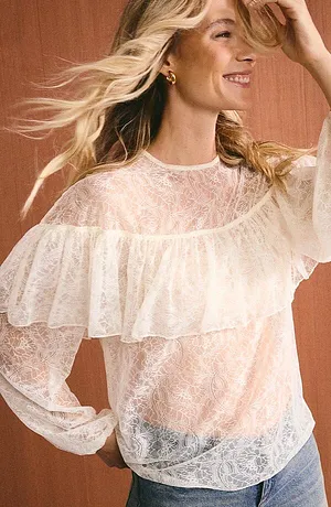 Blouse aérienne en dentelle avec volant et manches longues, associée à un jean décontracté pour un look féminin.