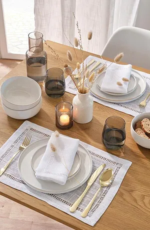Déco de table élégante avec un motif à dentelle, serviettes blanches en tissu et couverts couleur dorée pour une touche chic.