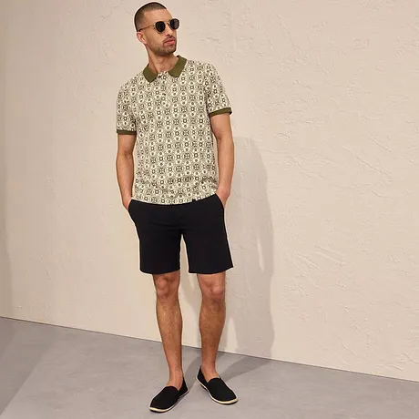 Le polo imprimé et le short foncé composent un look estival décontracté, des lunettes de soleil et des espadrilles finalisent la tenue.