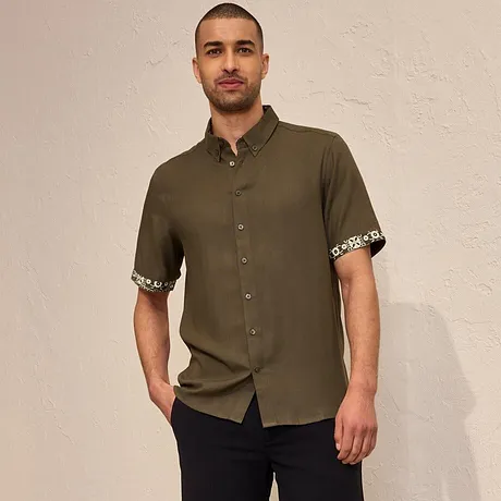 Chemise à manches courtes vert olive avec revers imprimé, short foncé et espadrilles noires.