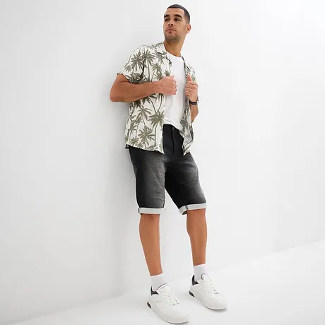Chemise hawaïenne estivale à motif plamiers, T-shirt blanc, short en jean gris et sneakers blanches.
