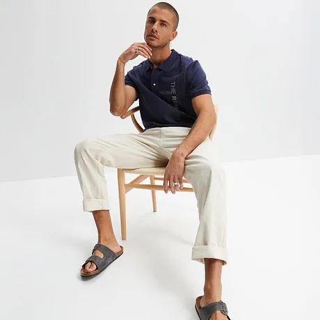 Polo bleu foncé, pantalon blanc et sandales grises. Un look estival et décontracté pour le quotidien. 