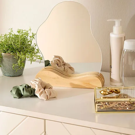 Accessoires de cheveux sur un meuble clair complété d'un miroir, d'une plante et de produits de beauté.