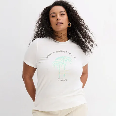T-shirt blanc à imprimé palmiers vert et inscription, associé à un pantalon clair.