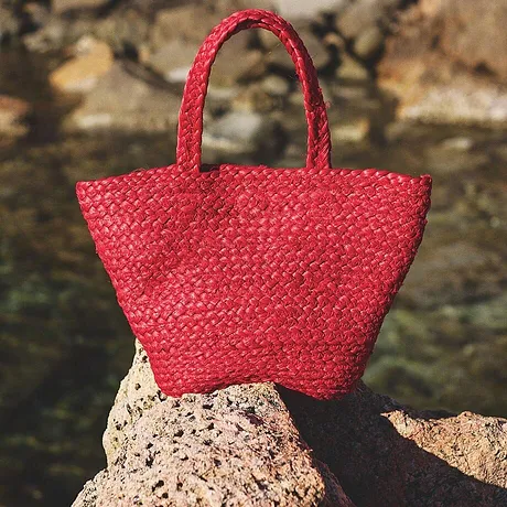 Sac en paille rouge lumineux posé sur un rocher au bord de l'eau, parfait pour vos escapades estivales.