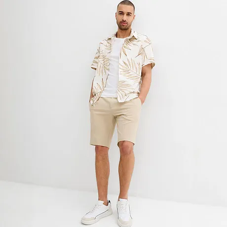 Tenue estivale composée d’un short beige et d’une chemise blanche à imprimé tropical.