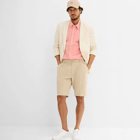 Veste crème élégante sur une chemise rose, sneakers blanches et casquette beige.