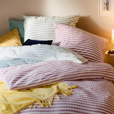 Des parures de lit rayées dans des tons pastel, le tout rehaussé par une couverture jaune pour une touche de couleur.