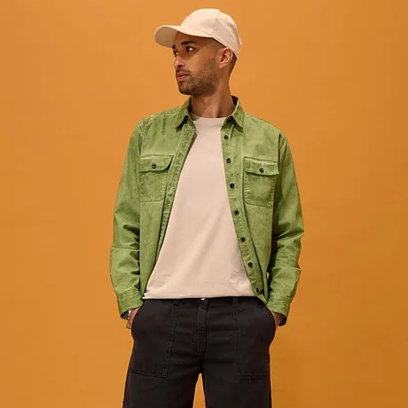 Chemise verte portée sur un T-shirt blanc, short foncé, sneakers blanches et casquette.