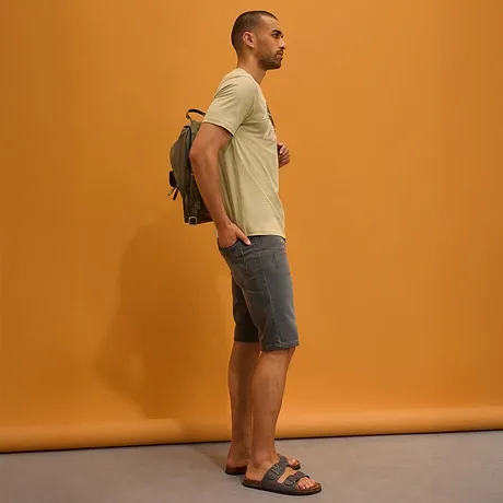T-shirt clair, short en jean gris, sandales et sac à dos.