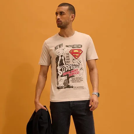 T-shirt blanc avec imprimé Superman, short foncé et sandales.