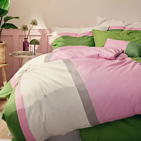 Une parure de lit aux couleurs fraîches (rose, vert et blanc) habille un lit confortable dans une chambre.