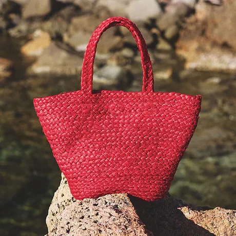 Sac en paille rouge vif posé sur des rochers au bord de l’eau, parfait pour les sorties à la plage.