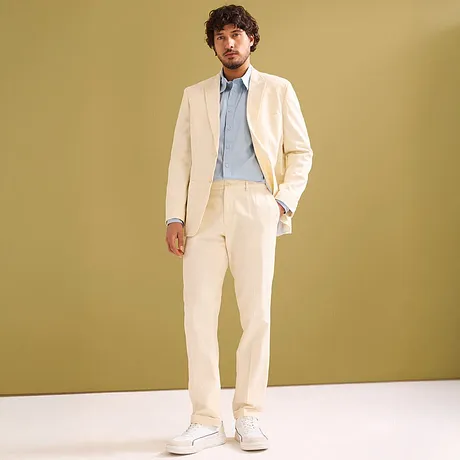 Costume élégant couleur crème avec chemise bleu clair et sneakers blanches.