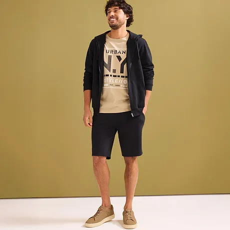 Look décontracté avec T-shirt beige, gilet noir à capuche & short en sweat foncé.