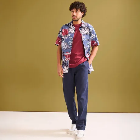 Chemise hawaïenne colorée sur un T-shirt rouge et un pantalon foncé.