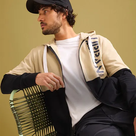 Look urbain : gilet beige, T-shirt blanc, pantalon foncé et casquette.