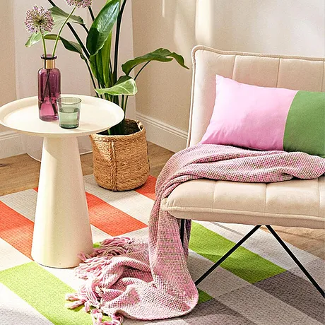 Des textiles en rose et vert pastel décorent un coin détente avec un plaid et un coussin sur un fauteuil.