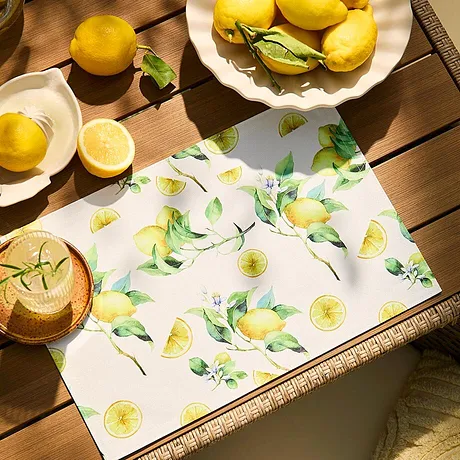 Un set de table à imprimé citron rafraîchissant décore la table, assorti aux fruits jaunes posés dessus.
