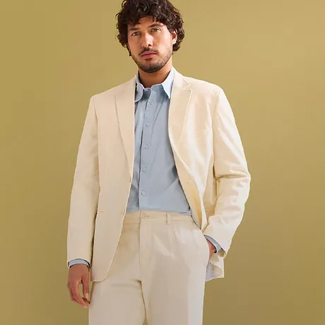 Costume élégant couleur crème avec chemise bleu clair et sneakers blanches.