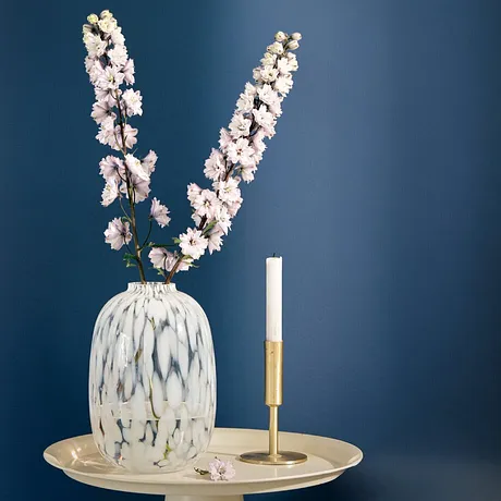 Vase blanc élégant avec branches de fleurs de cerisier sur un plateau couleur dorée, à côté d'une bougie chandelle.