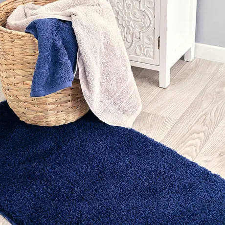Serviettes de toilette douces en coloris bleu et beige déposées dans un panier à linge sur un tapis moelleux. 