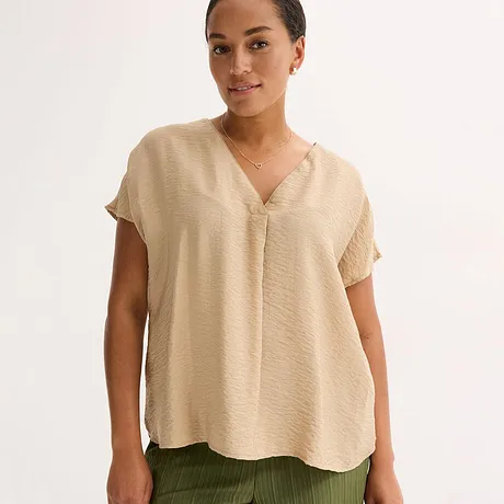 Blouse beige légère à encolure en V et manches courtes, associée à un pantalon vert olive.