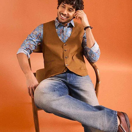 Gilet marron sans manches par dessus une chemise bleue à motifs, associé à un jean.