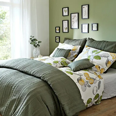 Chambre douillette avec parure de lit et coussins dans des tons verts. Le motif floral sur le linge de lit apporte de la fraîcheur.