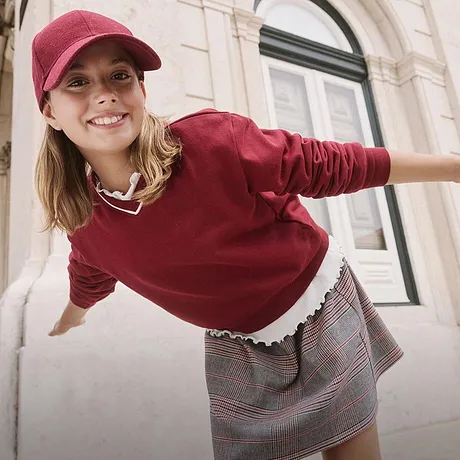 Pull rouge bourgogne et jupe à carreaux, complétés d'une jolie casquette rouge et petit collier.