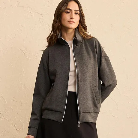 Veste style bombers de coloris gris avec fermeture zippée, associée à un top clair et une jupe noire.