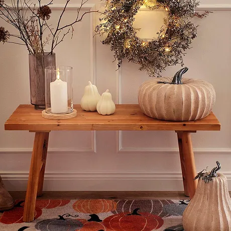 Décorations d'automne sur un banc en bois : couronne lumineuse, citrouilles et bougies créent une atmosphère conviviale. 