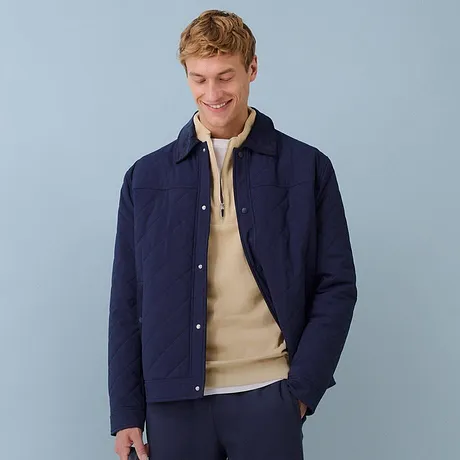 Veste matelassée bleu foncé associée à un pull de couleur beige et un pantalon bleu.