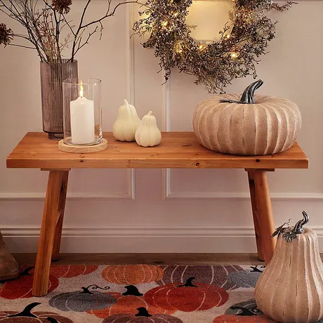 Décoration d'automne avec des citrouilles et une couronne, les teintes chaudes et les matières naturelles dominent. 