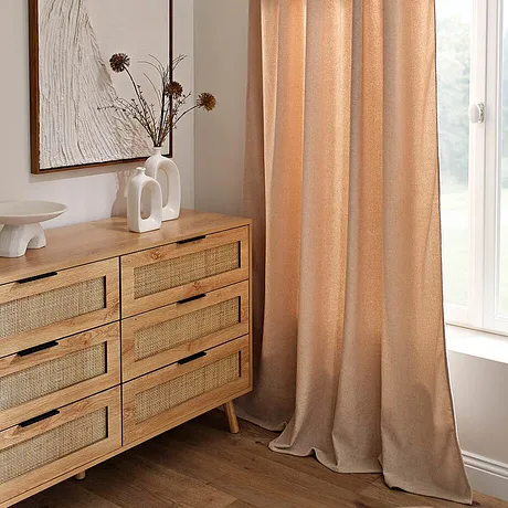 Des rideaux abricot habillent la fenêtre, en parfaite harmonie avec la commode en bois chaud. 