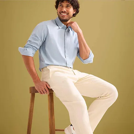 Chemise bleu clair avec manches retroussées, pantalon de costume beige.