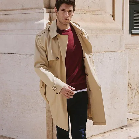 Trench-coat beige élégant par dessus un pull rouge et jean foncé.