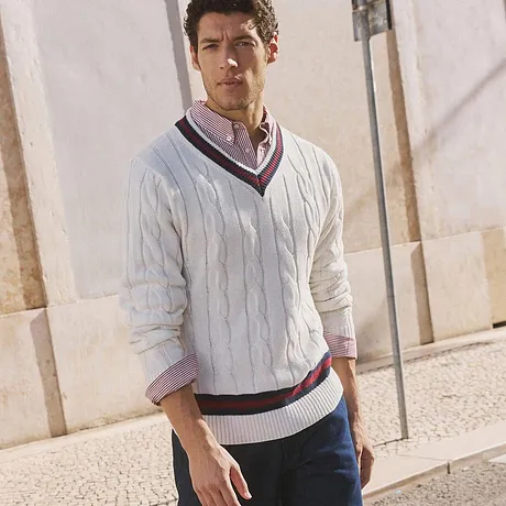 Pull en maille blanc à col en V, jean foncé et baskets blanches.