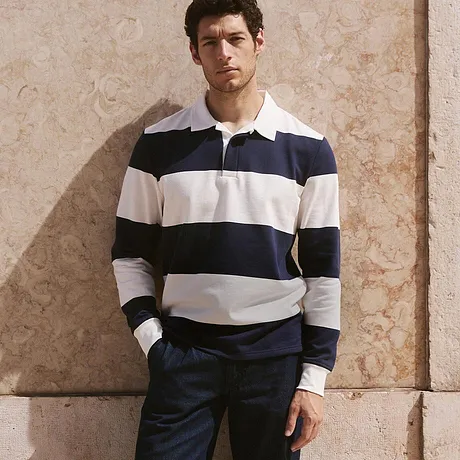 Look classique composé d'un sweat rugby rayé, pantalon foncé et baskets blanches.