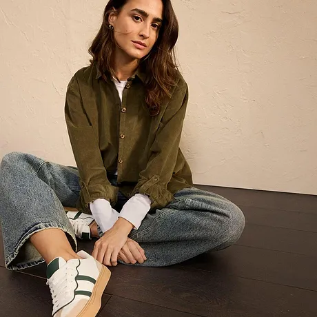 Veste vert olive, jean et baskets blanches à rayures vertes. 