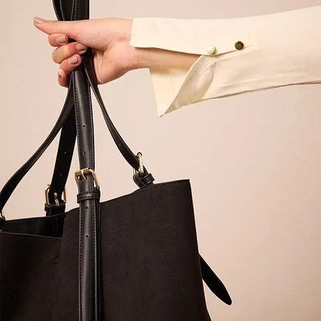 Une main qui tient un sac à main noir à longues anses.